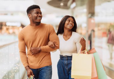 Binlerce yıllık güzel Afro-Amerikan erkek ve bayan hafta sonları alışveriş merkezinde renkli çantalarla dolaşırken, butik pencerelere bakarken ve birlikte gülerek vakit geçirirken portresi