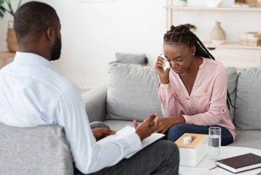 Depresyon danışmanlığı. Psikoterapide terapi seansında ağlayan mutsuz siyah kadın, sorunlarını paylaşan profesyonel terapist erkek, çaresiz kadına danışmanlık yapan, seçici odaklı