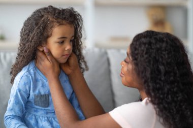 Aile anlaşmazlığı, çocukluk sorunları kavramı. Genç siyahi anne, üzgün, gücenmiş kızını evde tartıştıktan sonra teselli ediyor. Afrikalı Amerikalı bir kadın çocuğunu sakinleştiriyor.