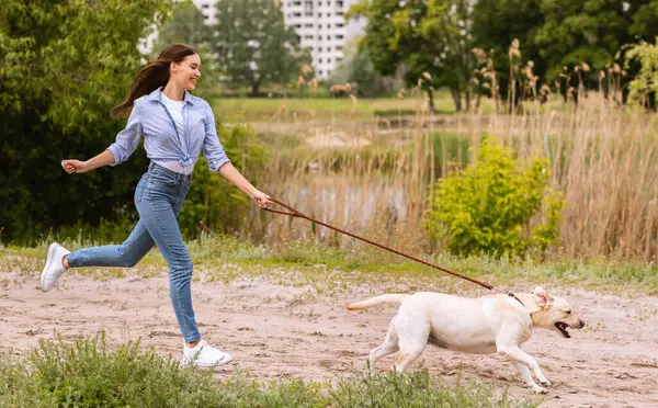 Aktif Hayvan Konsepti. Gülen kız gölün yanındaki parkta koşan köpeğini kovalıyor. Kopya alanı, tam boy yan manzara portresi.