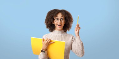 Eğitim ya da eğitim projesi için harika bir fikir. Gözlüklü, ağzı açık ve not defteri açık Afro-Amerikalı bir kadın, açık arka planda, panoramada, stüdyo çekiminde, boş alanda kalemi kaldırıyor.