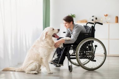 Evde köpeğiyle oynayan mutlu, engelli bir genç, boy boy portresi. Evcil hayvanıyla içeride iletişim kuran neşeli engelli ergen. Hayvan insan dostluğu kavramı