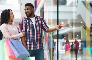 Sevgilisiyle alışveriş yapan, vitrindeki yeni kıyafetlere işaret eden, indirimli fiyatlar gösteren, sezonluk satışların keyfini çıkaran genç Afrikalı Amerikalı çift,