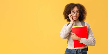 Heyecanlı insani duygular. Gözlüklü, ağzı açık, yüzüne karşı baskı yapan, Coronavirus karantinasından sonra not defterlerini tutan, sarı arka planda izole edilmiş Afrikalı Amerikalı kadın.