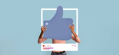 Bir kişi açık mavi bir arkaplan önünde online onayı sembolize eden büyük bir işaret tutar. Bu görüntü, içerik oluşturanlar için sosyal medya platformlarında etkileşimi teşvik eder.