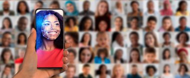 Yüz tanıma özelliğini gösteren akıllı telefonu tutan bir el. Arkasında, çeşitli yüzler kolajı modern kimlik teknolojisini sembolize eden çeşitli ifadeleri ve kimlikleri göstermektedir..