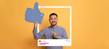 Neşeli bir içerik yaratıcısı parlak turuncu bir arkaplana karşı poz verir, başparmak işareti yapar..