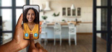 Evdeki sanal sohbete katılmak için akıllı telefonunu kullanan biri. Ortam, çevrimiçi iletişim deneyimini geliştiren sıcak bir atmosfere sahip modern bir mutfağa sahip..