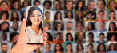 Bir el, yüz tanıma teknolojisini gösteren bir akıllı telefonu tutuyor. Cihaz, insanları çeşitli portrelerin kolajına karşı tarıyor ve modern tanımlama yöntemlerini eylem sırasında gösteriyor..