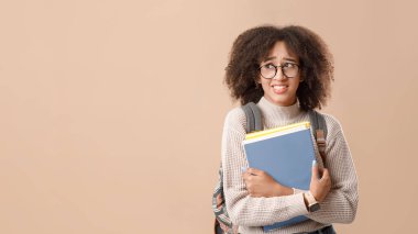 Yanlış bir şey ya da eğitimle ilgili bir sorun. Gözlüklü, sırt çantalı ve akıllı saatli üzgün Afro-Amerikalı kadın not defterleri tutuyor ve sarı arka planda izole edilmiş boş alana bakıyor.