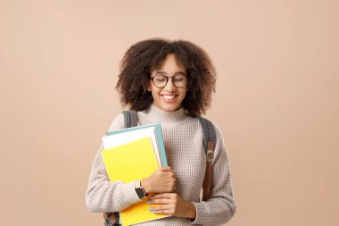 Utanç ve utangaçlığın doğal insani duyguları. Komik Afro-Amerikan bin yıllık gözlüklü kadın gülüyor, not defteri tutuyor ve sarı arka planda izole bir şekilde okula dönüyor.