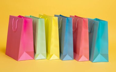 Değişik renklerde alışveriş torbaları sarı arka planda göze çarpıyor. Çantalar boy ve ton olarak farklılık göstererek, alışveriş promosyonları için ideal bir vitrin oluşturuyor..