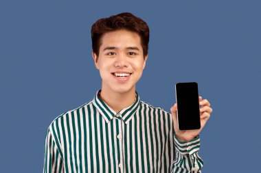 Bu web sitesini tavsiye ediyorum. Elinde siyah boş ekranla akıllı telefonu tutan gülümseyen Asyalı genç adam kameraya gösteriyor. Model için boş alanı olan Gadget, mor stüdyo arkaplanı üzerine izole edilmiş