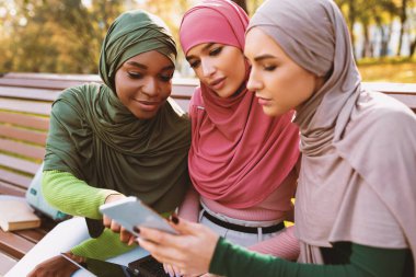 Yeni Eğitim Uygulaması ile Akıllı Telefon kullanan İslami Kadın Öğrenciler Kampüs Parkı 'nda Bench' te birlikte oturarak Öğreniyorlar. People and Gadgets, Modern Eğitim Konsepti. Seçici Odaklanma