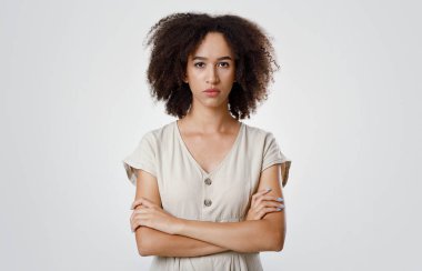 Kızgınlık ve üzüntü, duygular ve yüz ifadeleri. Katı bir şekilde binlerce yıllık Afro-Amerikan kıvırcık kız öğrenciyi gücendirdi. Kollarını kavuşturdu ve gri arka planda izole bir şekilde kameraya baktı.