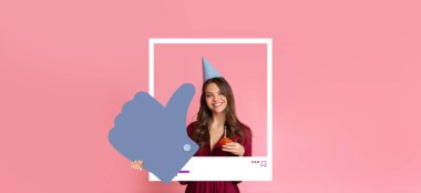 Parti şapkası takan genç bir kadın elinde şeker tutarken gülümsüyor pembe arka plan önünde baş parmak işareti gösteriyor. Çevrimiçi izleyicileri için neşeli bir an yakalıyor..