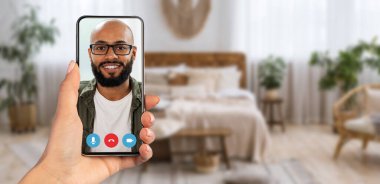 Bir insan akıllı telefonunda gülümseyen bir şahısla görüntülü görüşme yapmaktan zevk alır. Bitkilerle dolu rahat bir ev ortamı ve hoş bir dekor sunar..