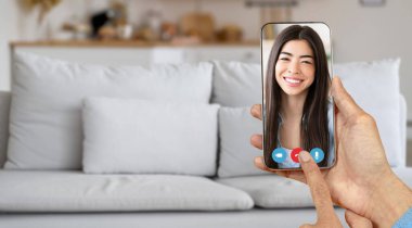 Bir insan evde otururken akıllı telefon kullanarak arkadaşça bir video görüşmesi yapar. Arka planda modern telekomünikasyonun resmedildiği rahat bir kanepe var..