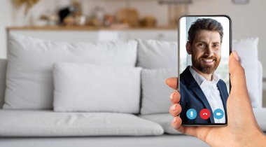 Kişi, rahat bir evde akıllı telefon kullanarak çevrimiçi sohbet ediyor. Yumuşak mobilyaları olan parlak bir oturma odası sohbet ederken rahat bir atmosfer yaratır..