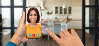 Konforlu evindeyken canlı bir görüntülü konuşma yapmak için bir akıllı telefon tutan bir kişi var. Arka planda iyi aydınlatılmış bir mutfak ortamı var. Bağlantı atmosferini arttırıyor..