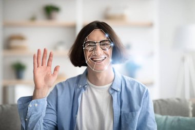 Evde yüz tanıma teknolojisini tecrübe ederken neşeli bir yüz ifadesi dalgası olan bir insan. Bu, modern teknolojinin günlük yaşamdaki entegrasyonunu gösteriyor, kişisel etkileşimi vurguluyor.