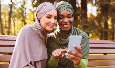 Modern Müslüman Kadın, Parkta Bankta Oturan Kadın Arkadaş İçin Akıllı Cep Telefonu Uygulaması Öneriyor. Sosyal Medya Uygulamasını Telefonla Kullanan İki Arap Kadın Ağı. Seçici Odaklanma