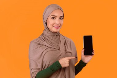 Harika Mobil Uygulama. Smartphone Boş Ekranı Gösteren Müslüman Kadın Sarı Stüdyo Arkaplanındaki Yeni Telefon Uygulama Pozisyonu Tavsiye Ediyor. İslam Kadını Cep Telefonu Uygulamalarını Onaylıyor. Model