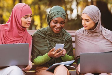 Arkadaşlarıyla Çevrimiçi Akıllı Telefonlu Müslüman Bayan Kampüs Parkı 'nda yan yana oturan dizüstü bilgisayarları kullanıyor. Eğitim Başvurusu, Uzaktan Eğitim ve E-Öğrenim Konsepti
