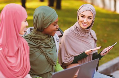 Modern Müslüman Öğrenci Bayan Akıllı Telefon Mobil Uygulamasını Tavsiye Ediyor Açık havada dizüstü bilgisayarlarla bankta oturan arkadaşlara. Telefon için Eğitim Başvurusu. Seçici Odaklanma