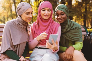Bir grup Müslüman Öğrenci Dışarıda Eğitim Uygulaması Öğrenen Cep Telefonu Kullanıyor. Hijab 'daki İslami Kadınlar parkta internet üzerinden cep telefonlarına bakıyorlar. Harika bir uygulama. Seçici Odaklanma