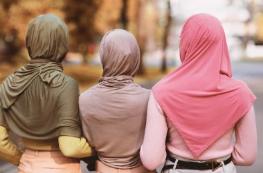 Geleneksel türbanlı tanınmayan üç Müslüman kadın şehir parkındaki kameraya doğru yürüyorlar. Kadın Arkadaşlığı ve Moda Konsepti. Arka Görünüm