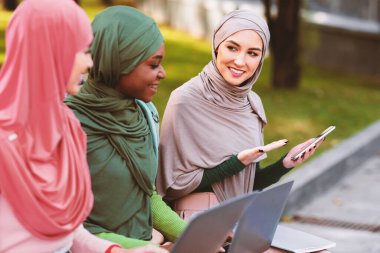 Çağdaş Müslüman Bayan Öğrenci Dışarıda Park 'ta Öğrenen Bankta oturan Arkadaşlarına Eğitici Cep Telefonu Uygulaması Tavsiye Ediyor. Uzaktan Eğitim Başvurusu, E-Öğrenme. Seçici Odaklanma