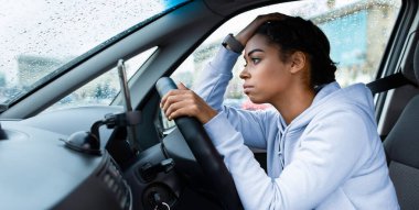 Yağmurlu hava, yolda sorunlar ve trafik sıkışıklığı. Bin yıllık üzgün Afrikalı Amerikalı kadın direksiyonda akıllı bir şekilde, elleri kafasında, ıslak pencereye, yan manzaraya, boş alana bakıyor.