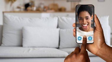 Bir insan arkadaşıyla çevrimiçi bir video görüşmesi yapar, akıllı telefon kullanır, konuşurken gülümser. Rahat ev ortamları bu sanal iletişimdeki bağlantıyı güçlendirir.