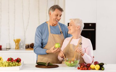 Happy Senior Couple Cooking Together Preparing Healthy Dinner In Modern Kitchen At Home. Elderly Spouses Making Fresh Vegetable Salad Indoor. Family Recipes, Nutrition In Older Age Concept