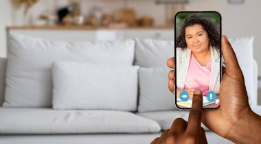 Bir kişi elinde bir akıllı telefon tutuyor ve bir arkadaşıyla görüntülü konuşma yapıyor. Konforlu ev ortamında rahat bir kanepe, gündelik iletişim ve bağlantının vurgulanması.