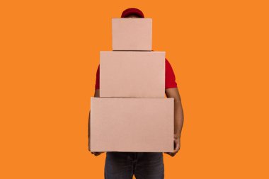 En iyi servis konsepti. Kırmızı, biçimsiz, turuncu stüdyo arka planında izole bir şekilde duran karton kutular taşıyan tanınmamış bir kara teslimatçı. Afro-Amerikan kurye paketleri taşıyor.