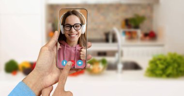 Evdeki bir kişi video bağlantısı kurmak için akıllı telefon kullanıyor. Mutfak arka planı, telekomünikasyon deneyimine canlı bir dokunuş katıyor..