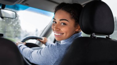 Şirin şoför, otomobil blogcusu ve arkadaşlarıyla seyahat ediyor. Gülümseyen genç Afro-Amerikan kadın arka koltuğa döner ve yolcu veya müşteriyle konuşur, yağmur damlalı pencere manzarası, kopyalama alanı