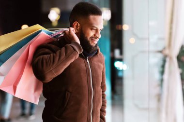 Alışveriş zamanı. Ortadaki alışveriş merkezinin vitrinine bakan gülümseyen siyah sakallı adamın portresi. Dışarıda duran, çantalarını taşıyan neşeli yakışıklı adam. Mevsimlik Satış, Teklif ve İndirim