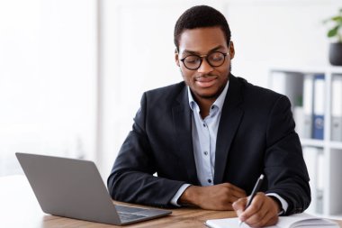 Hevesli bir siyahi işadamı gününü modern dizüstü bilgisayarın önünde oturup not defterine yazarak geçirmeyi planlıyor. Genç Afrikalı Amerikalı yönetici çevrimiçi eğitim alıyor, notlar alıyor.