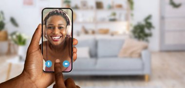 Akıllı telefon kullanarak görüntülü konuşma yapan biri ekranda gülümseyen bir yüz gösterir. Parlak bir dekor ve rahat bir kanepe sıcak bir ev atmosferi yaratarak bağlantıyı güçlendirir..