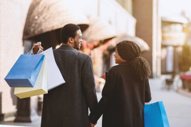 Sonbahar ve kara cuma, sezon indirimi ve tatil. Bir sürü renkli kesekâğıdı taşıyan mutlu Afro-Amerikan erkek ve kadın alışverişten sonra sokağa çıkıp birbirlerine bakıyorlar.