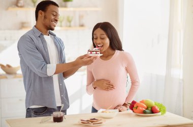 Pozitif Afro-Amerikalı bir adam hamile kız arkadaşına lezzetli bir kek ikram ediyor. Çekici siyahi adam, müstakbel karısını mutfakta lezzetli bir tatlıyla baştan çıkarıyor. Kötü hamilelik diyeti kavramı