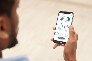 Akıllı telefonda analitik mobil uygulama kullanan siyah bir adam borsa ve panorama gelirlerini kontrol ediyor. En yeni analitik mobil uygulamalı erkek eller telefonu tutuyor