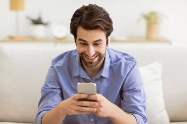 Evdeki koltukta oturan ve kulaklık takan cep telefonuyla video görüşmesi yapan mutlu adam. Modern Uzaktan İletişim. Teknoloji ve Gadget, Mobil Uygulama Konsepti
