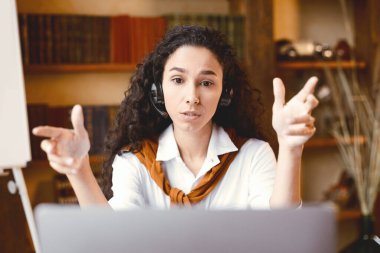 Uzaktan kumanda. Masada oturan odaklanmış bir kadının portresi, dizüstü bilgisayarında video görüşmesi, öğrencilere dersi açıklamak veya çalışmak ve iş arkadaşlarıyla konuşmak ve webcam 'e el kol hareketi yapmak,