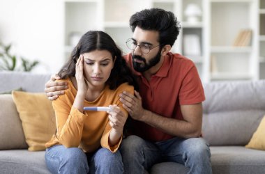 Kısırlık sorunları. Negatif hamilelik testine bakan üzgün Hintli genç çiftin portresi evde birlikte otururken, Doğu kocasını önemseyen depresif eş, boş alan.