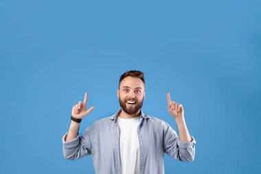 Heyecanlı sakallı adam mavi stüdyo arka planındaki boşluğu işaret ediyor. Yakışıklı milenyum adamı harika bir teklif sunuyor, satış ya da indirim öneriyor, ürününüzün reklamını yapıyor.