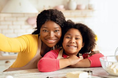 Mutlu Afrikalı anne küçük kızıyla mutfakta selfie çekiyor. Neşeli siyah anne ve çocuk önlük takıyor, poz veriyor ve kameraya gülümsüyor evde birlikte yemek pişirirken, yakın çekim